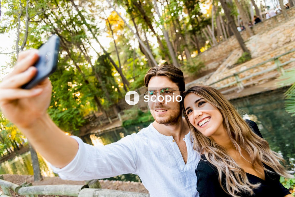 Smiling man and woman standing and taking photo near body of water