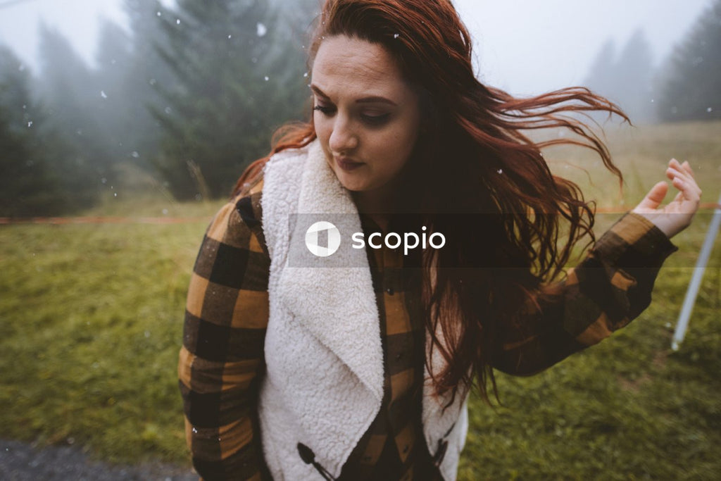 Portrait of woman with red hair standing on grass field near forest looking away