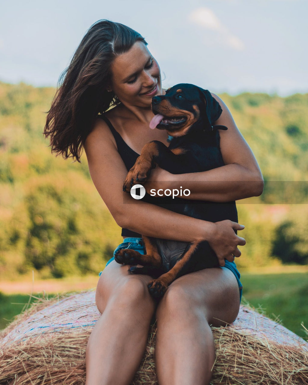 Woman in blue tank top hugging black and brown short coated dog