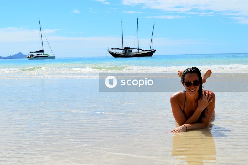 Woman in black bikini wearing black sunglasses sitting on beach