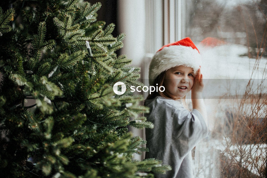 Girl in Christmas hat standing beside green Christmas tree