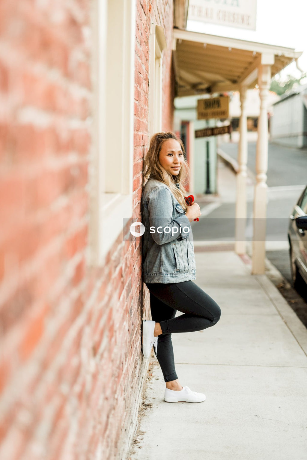 Side view of woman in denim jacket leaning on a red brick wall