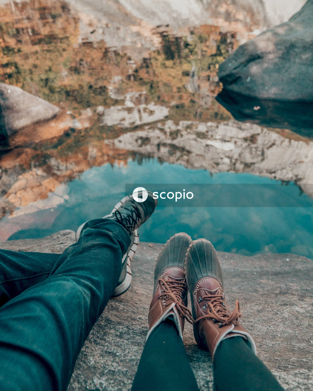 Person in blue denim jeans and brown hiking shoes sitting on rock