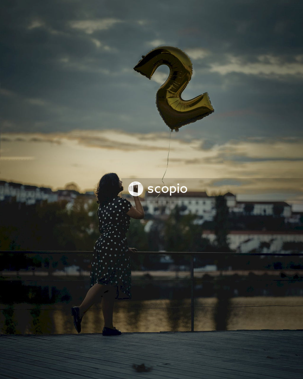 Woman in black and white polka dot dress holding yellow and brown heart balloon