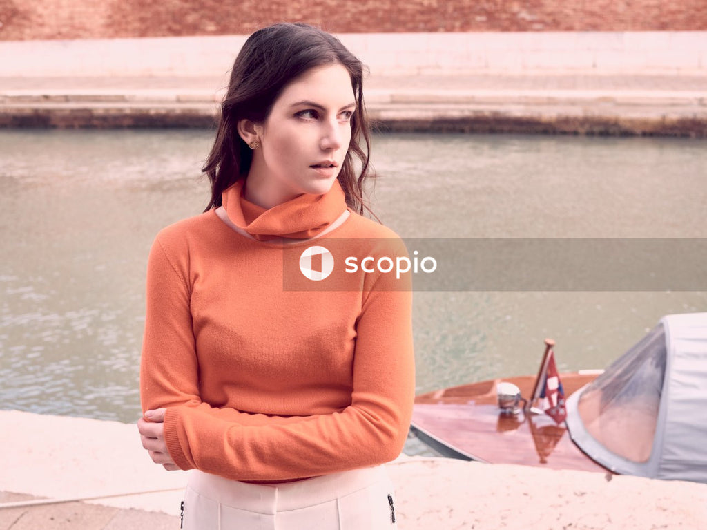 Woman wearing orange long-sleeved top leanin on beige surface near boat on river