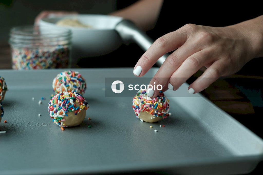 Person pouring sprinkles on cupcakes