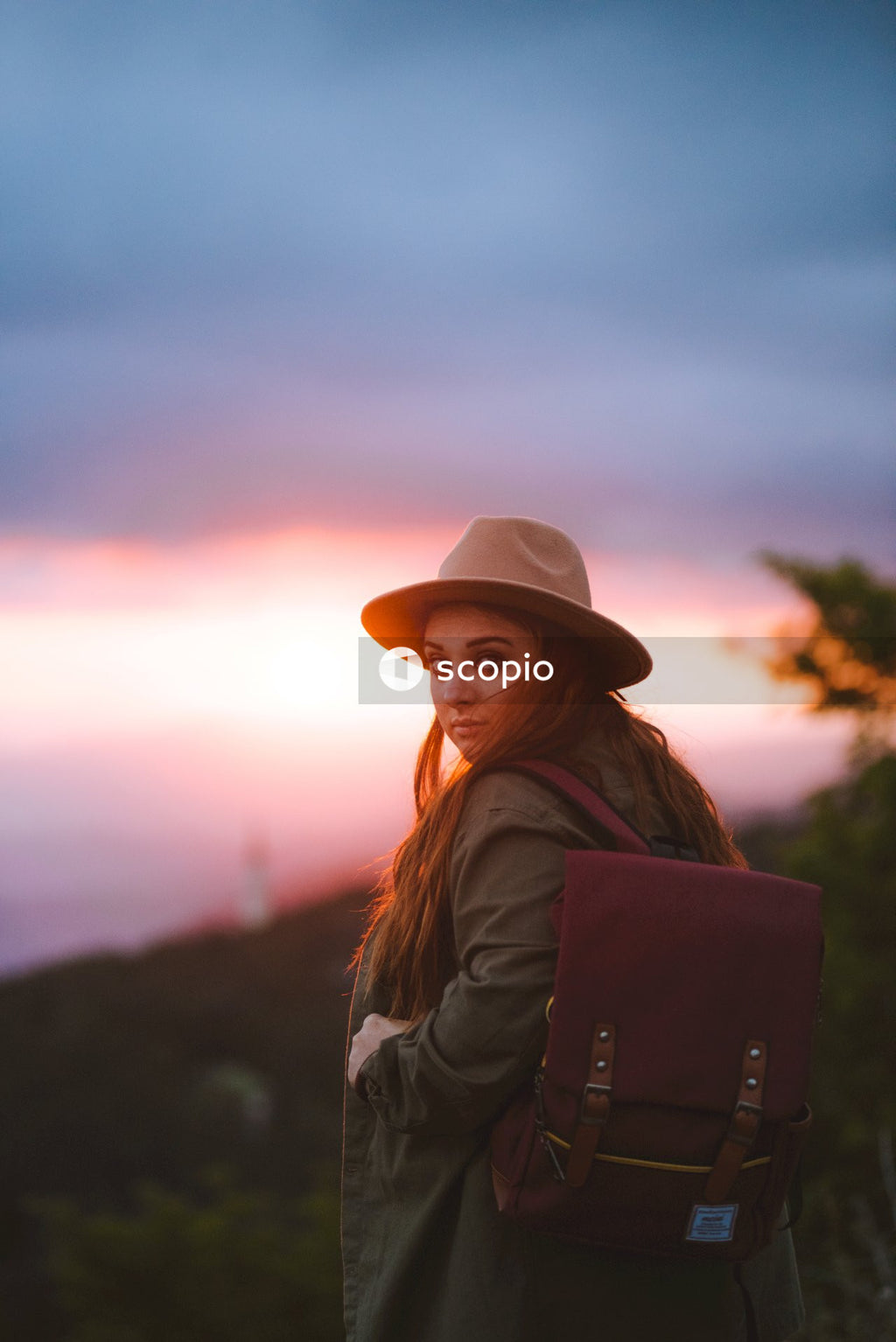 Back view of woman with leather bag and fedora hat standing outdoor at sunset