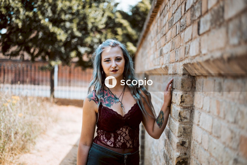 Woman in black and red floral tank top standing beside brown brick wall