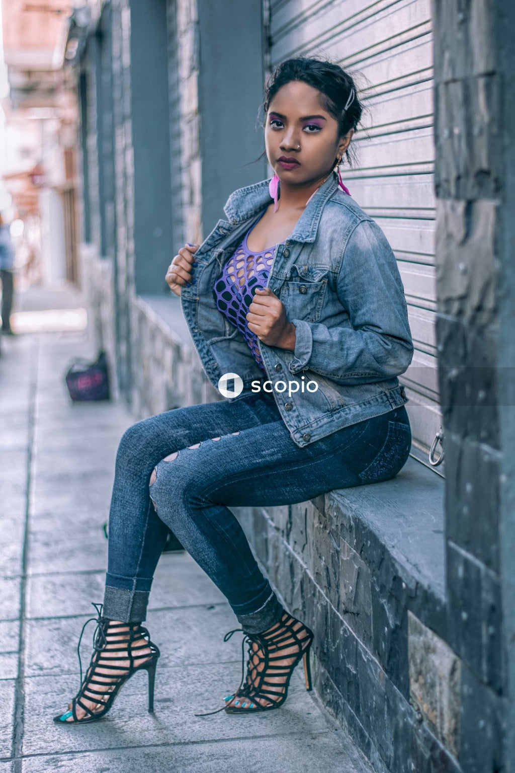 Woman in blue denim jacket and blue denim jeans sitting on concrete wall
