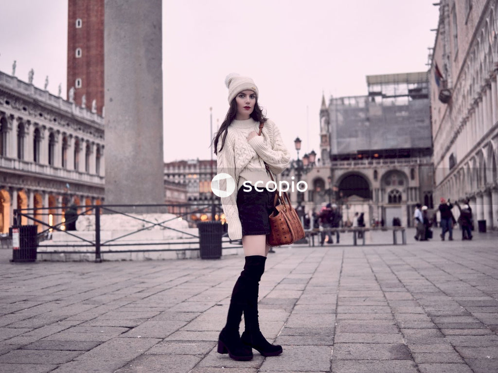 Woman in white knit sweater and black miniskirt with black thigh boots outfit standing on gray concrete floor