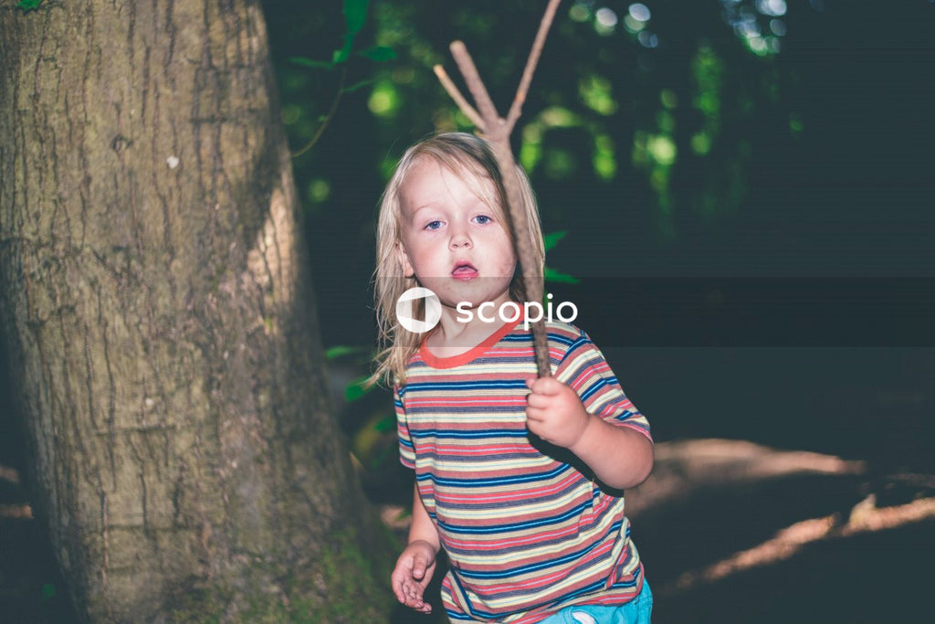 Girl in red and white striped shirt standing beside tree