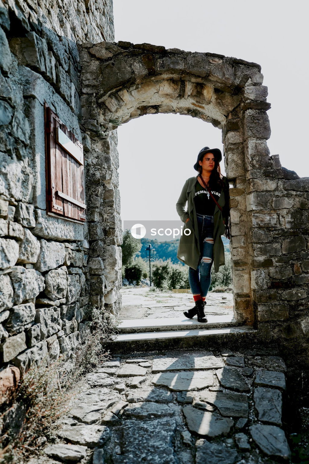 Woman in brown jacket and blue denim jeans standing on gray concrete tunnel