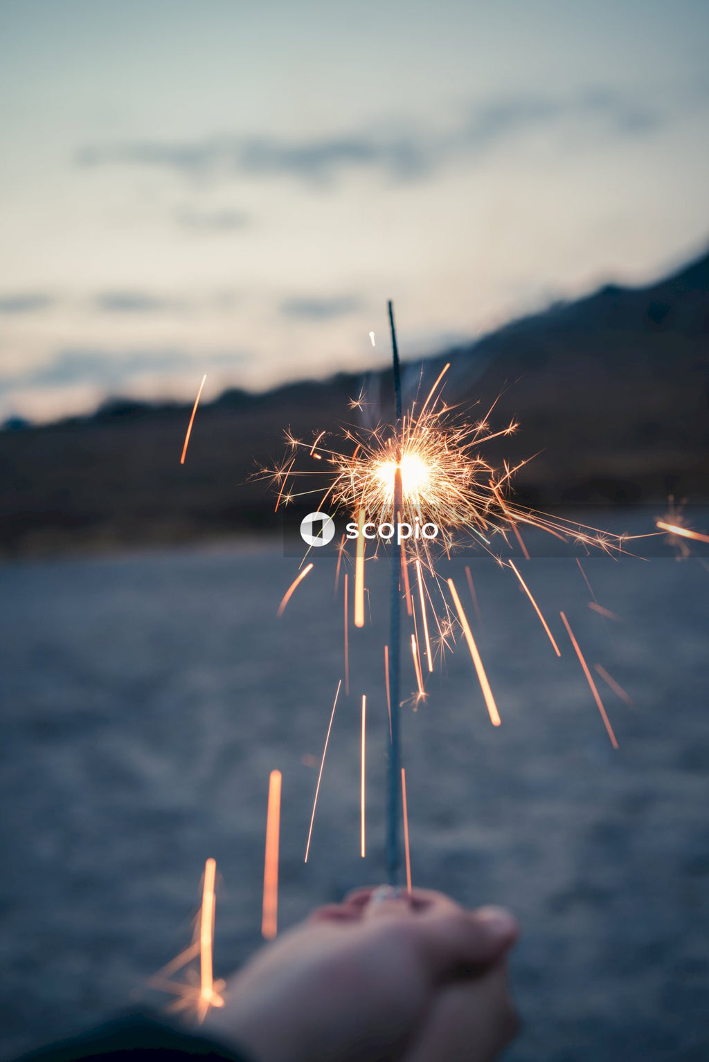 Person standing near the ocean holding sparkling lights