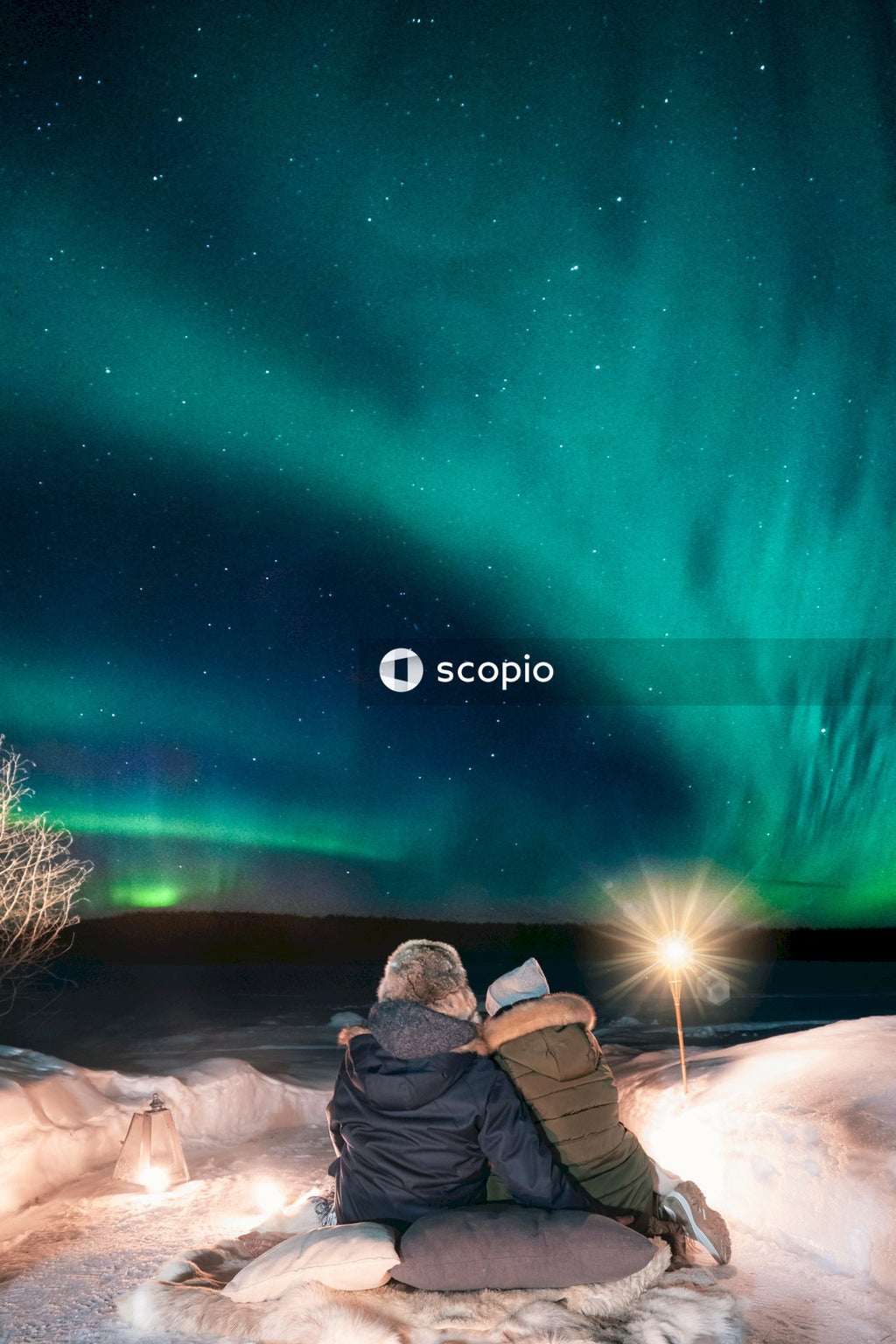Two people sitting on ground under aurora borealis at nighttime