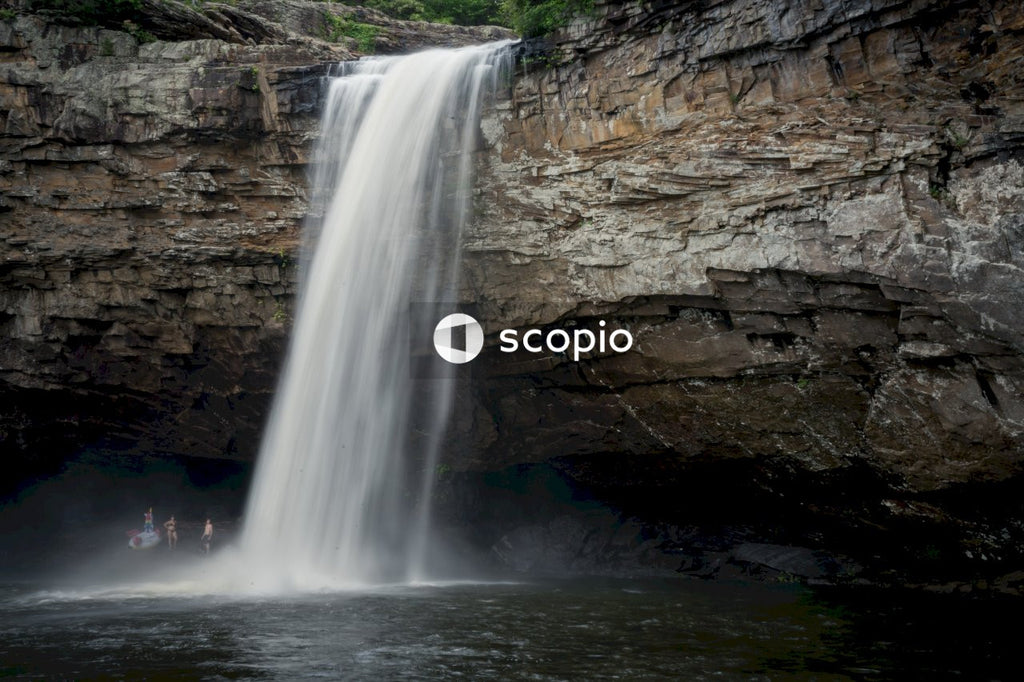 Water fall on brown rocky mountain with people under it