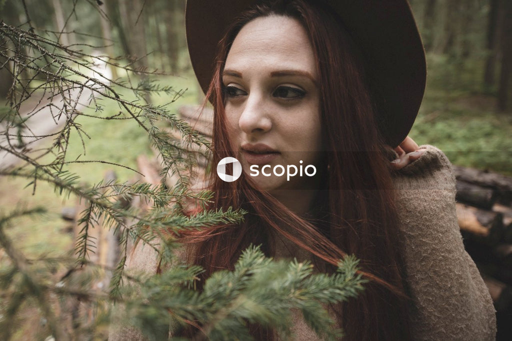 Woman with red hair wearing a dark hat standing beside tree