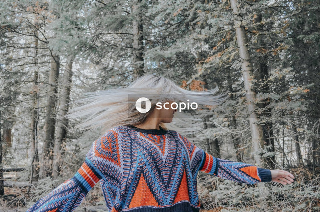 Woman in blue and red sweater standing near trees