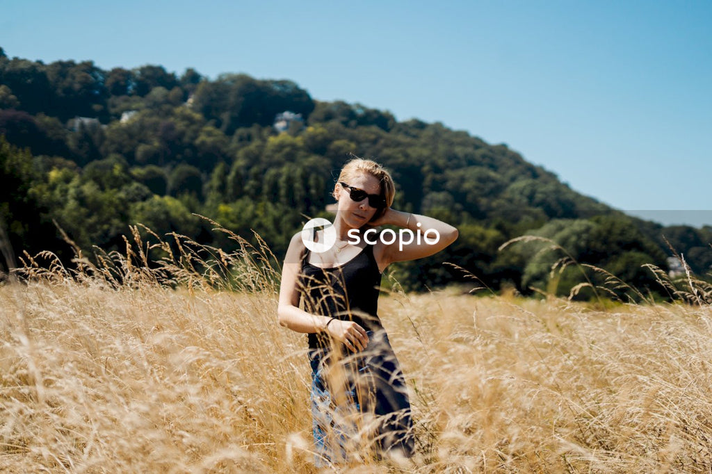 Woman in black tank top and white and blue floral skirt standing on brown grass field