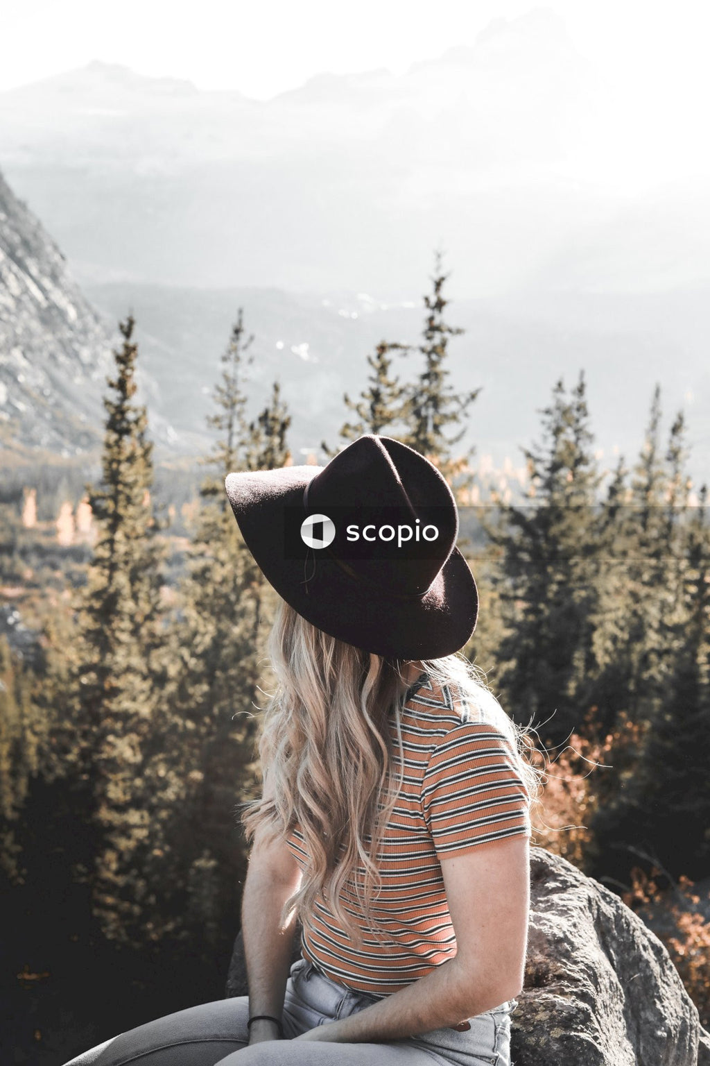 Woman in black fedora hat standing near green trees