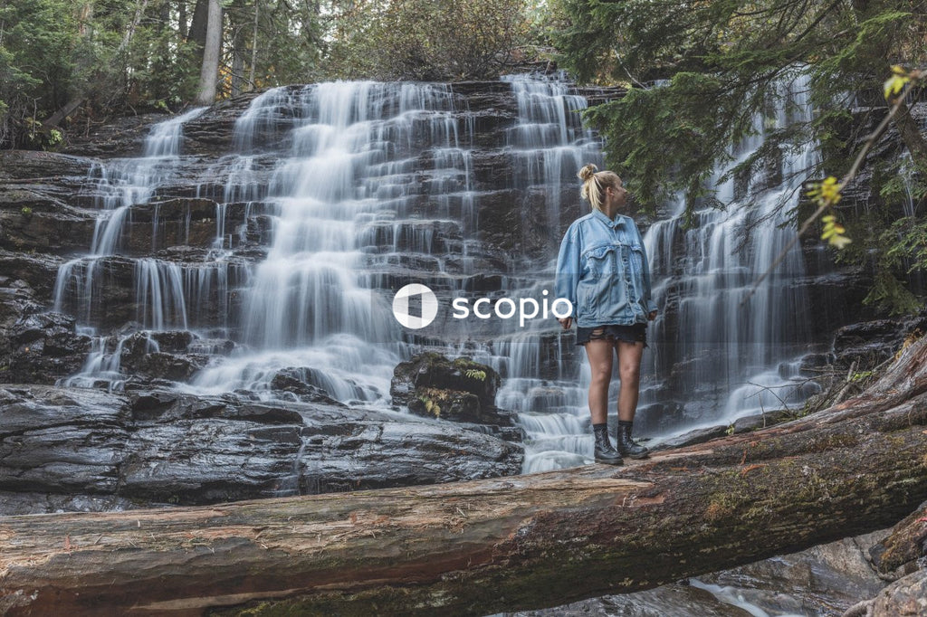 Man in blue denim jacket standing on rock in front of waterfalls