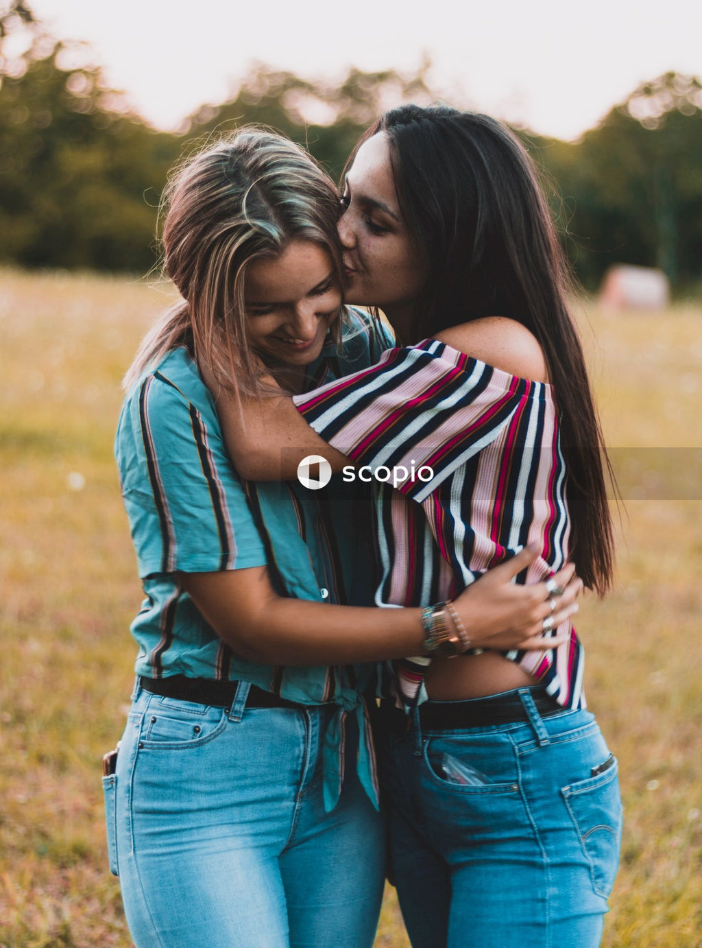 Woman in blue denim jacket hugging woman in white red and blue striped shirt