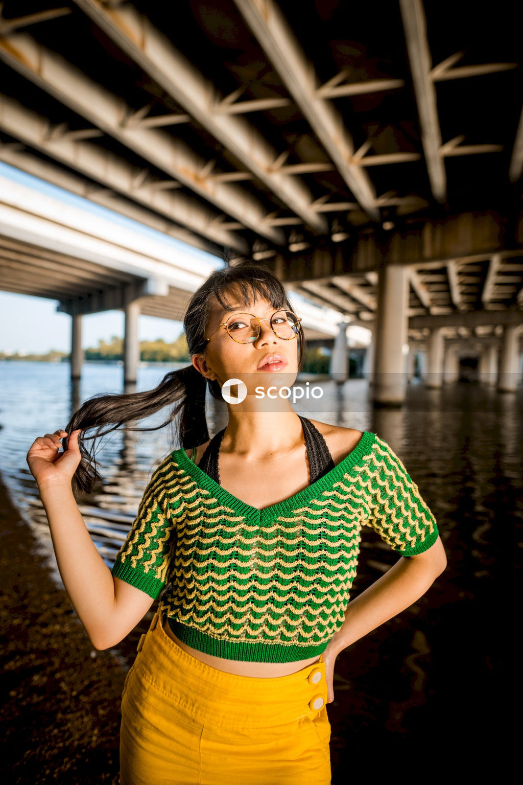 Woman in green shirt standing under dock at the beach
