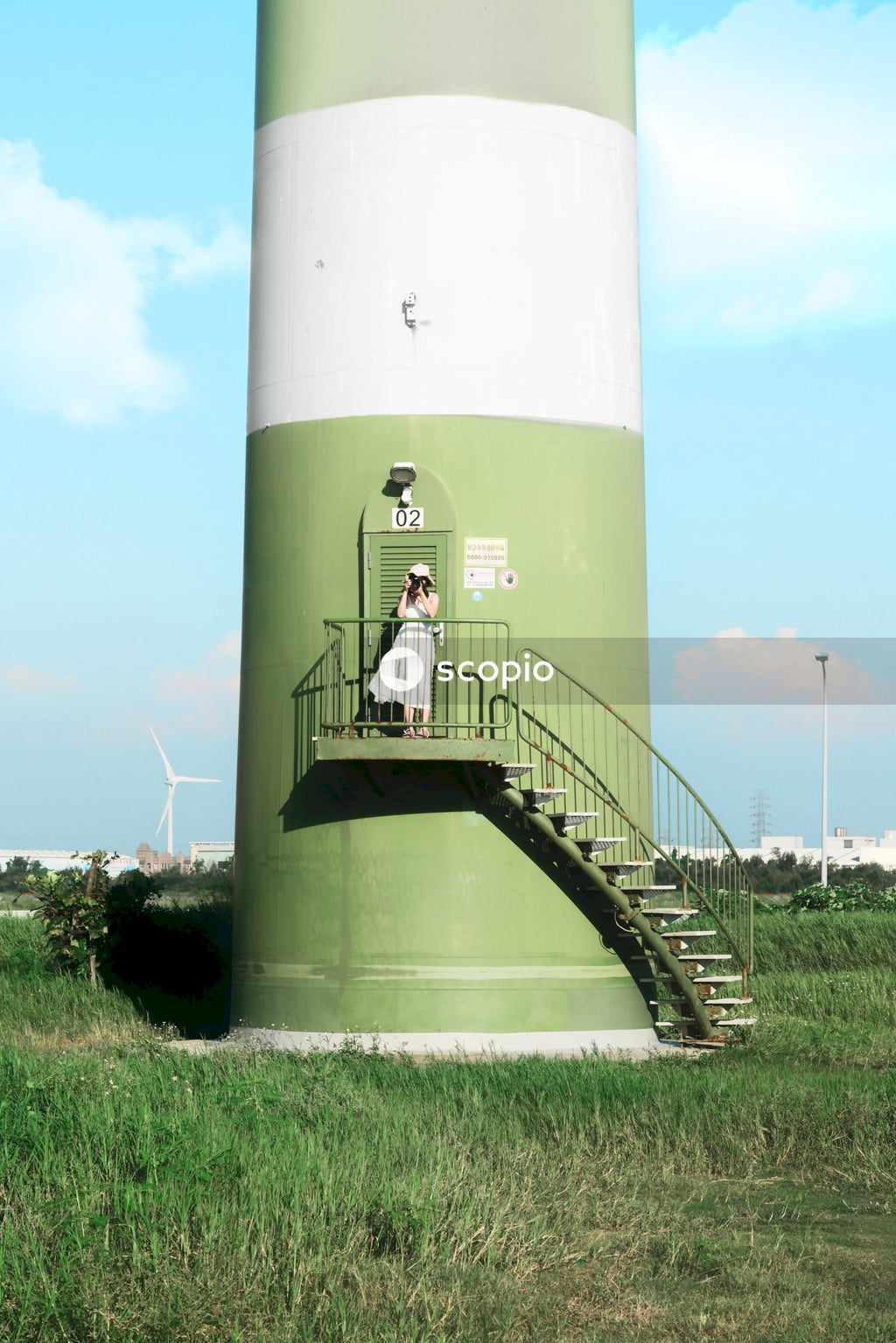 Woman in light dress standing at green lighthouse in front of wind turbines