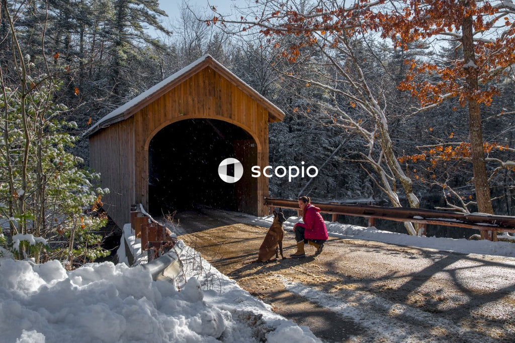 Man in red jacket and black pants sitting on brown wooden bridge