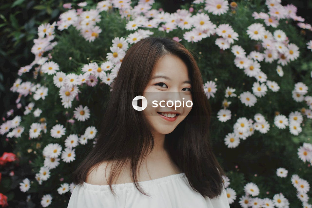 Smiling girl in light top standing in front of flowers