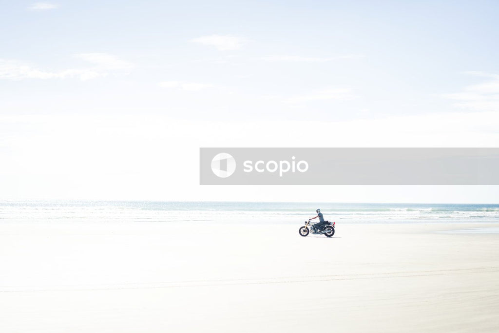 Person motorcycling on white sand across the ocean