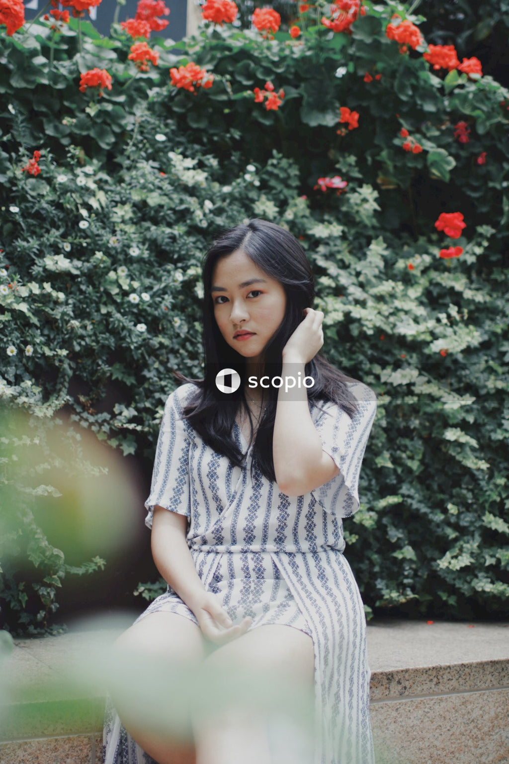 Woman in long light and blue stripped dress posing near bushes and flowers