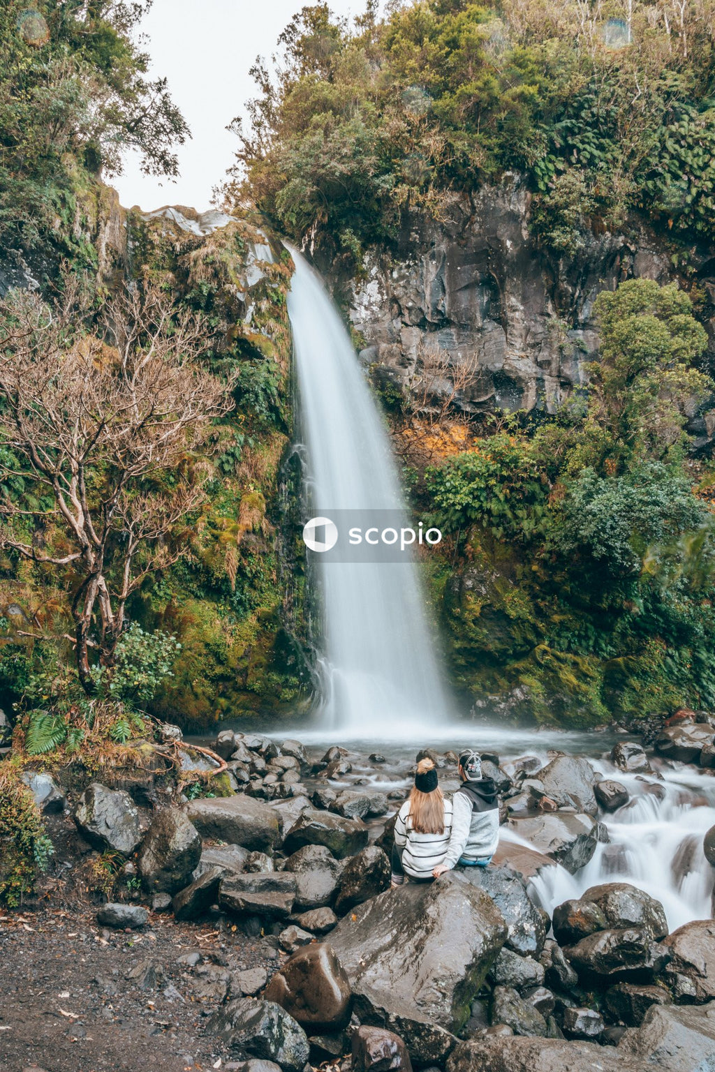 Man and woman sitting on rock facing on waterfall