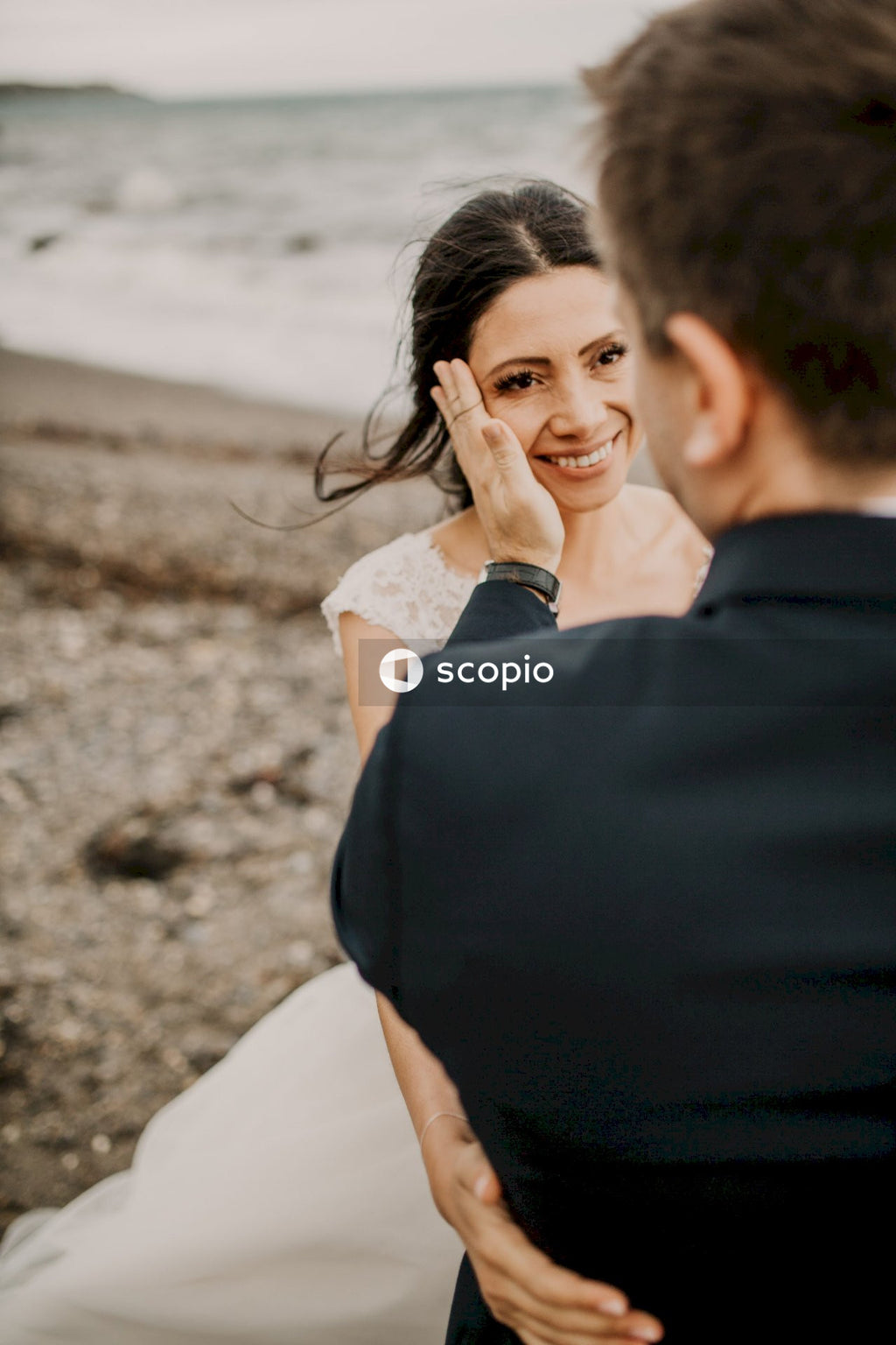 Man in black suit kissing woman in white dress on beach