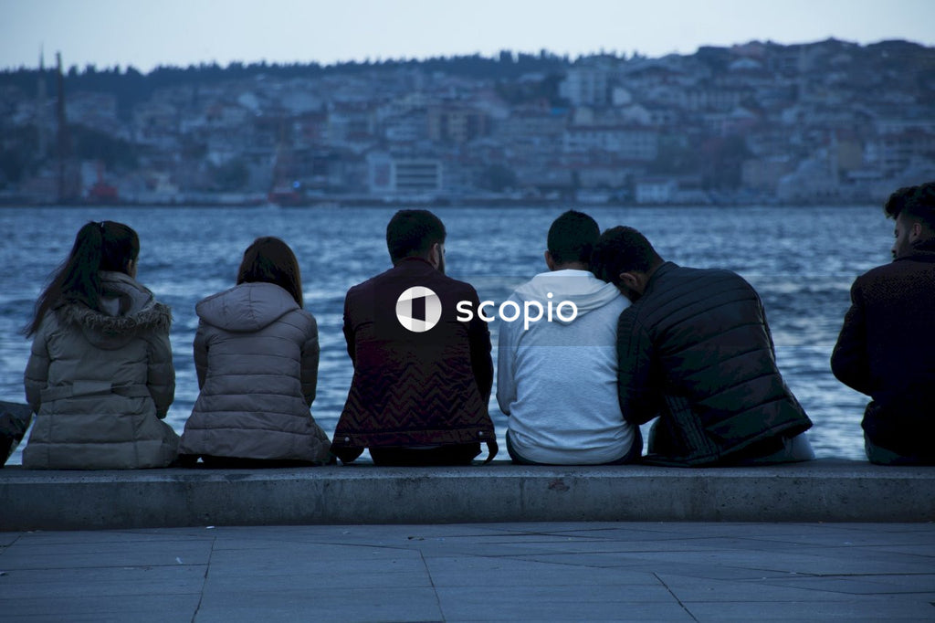 Back view of young people sitting wooden bench looking at the sea