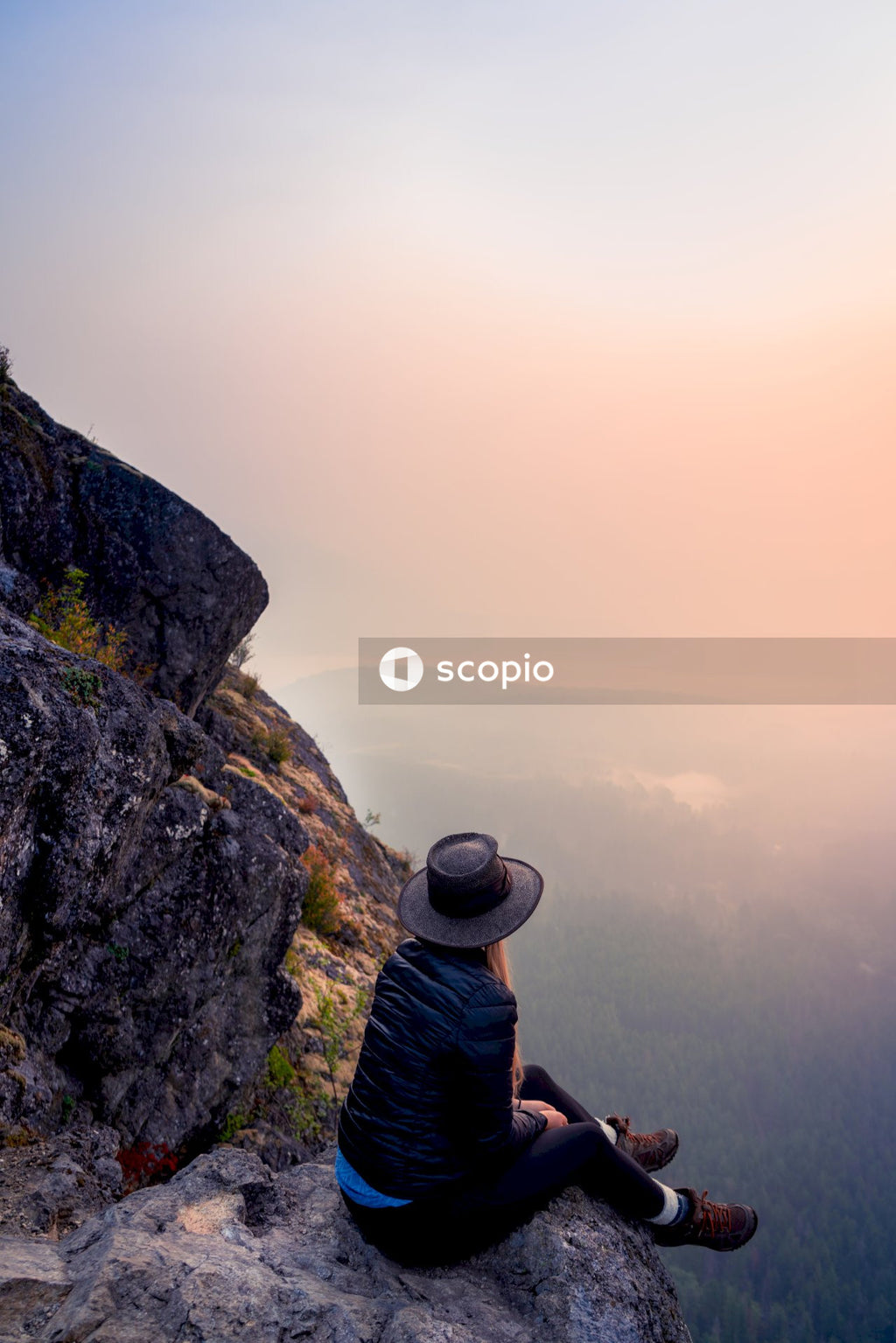 Woman sitting on rock formation and looking at the ocean