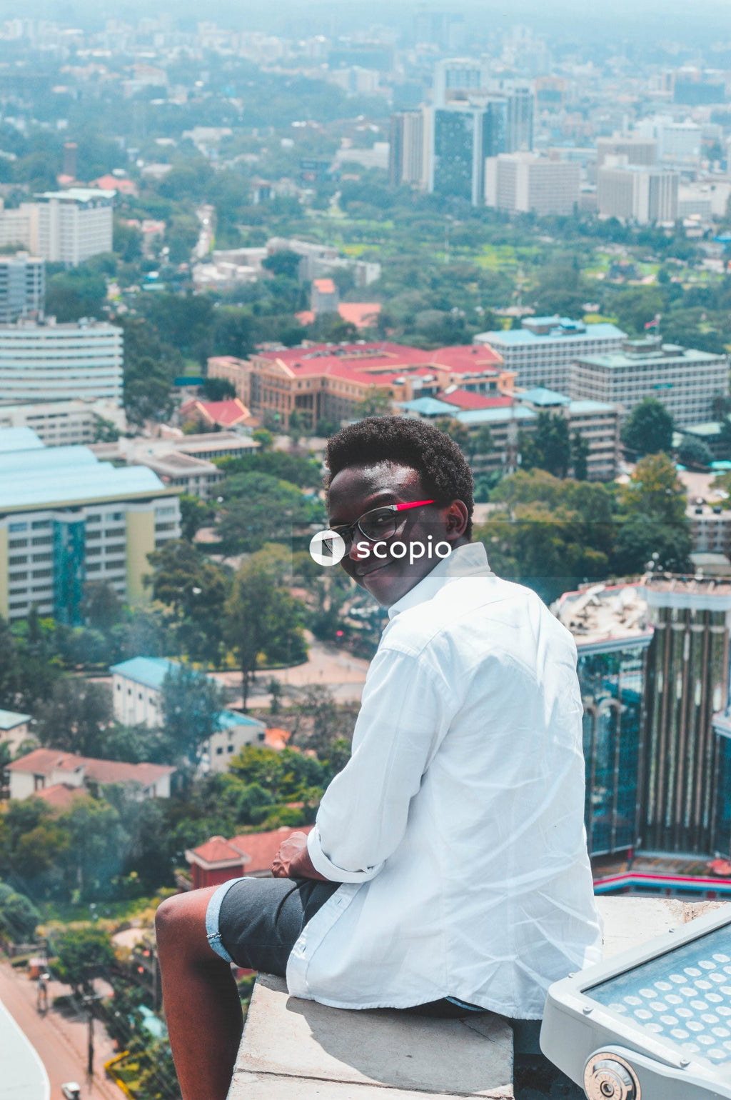 Back view of young African man sitting on top of building looking down the city