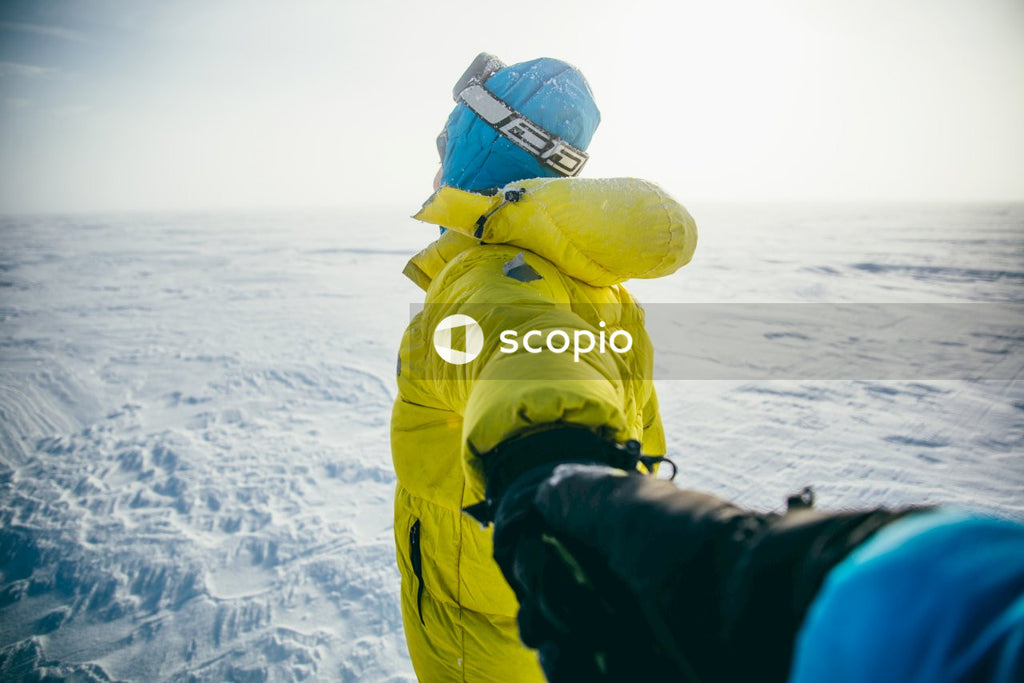Person in yellow jacket holding a hand of another person near snow covered ground
