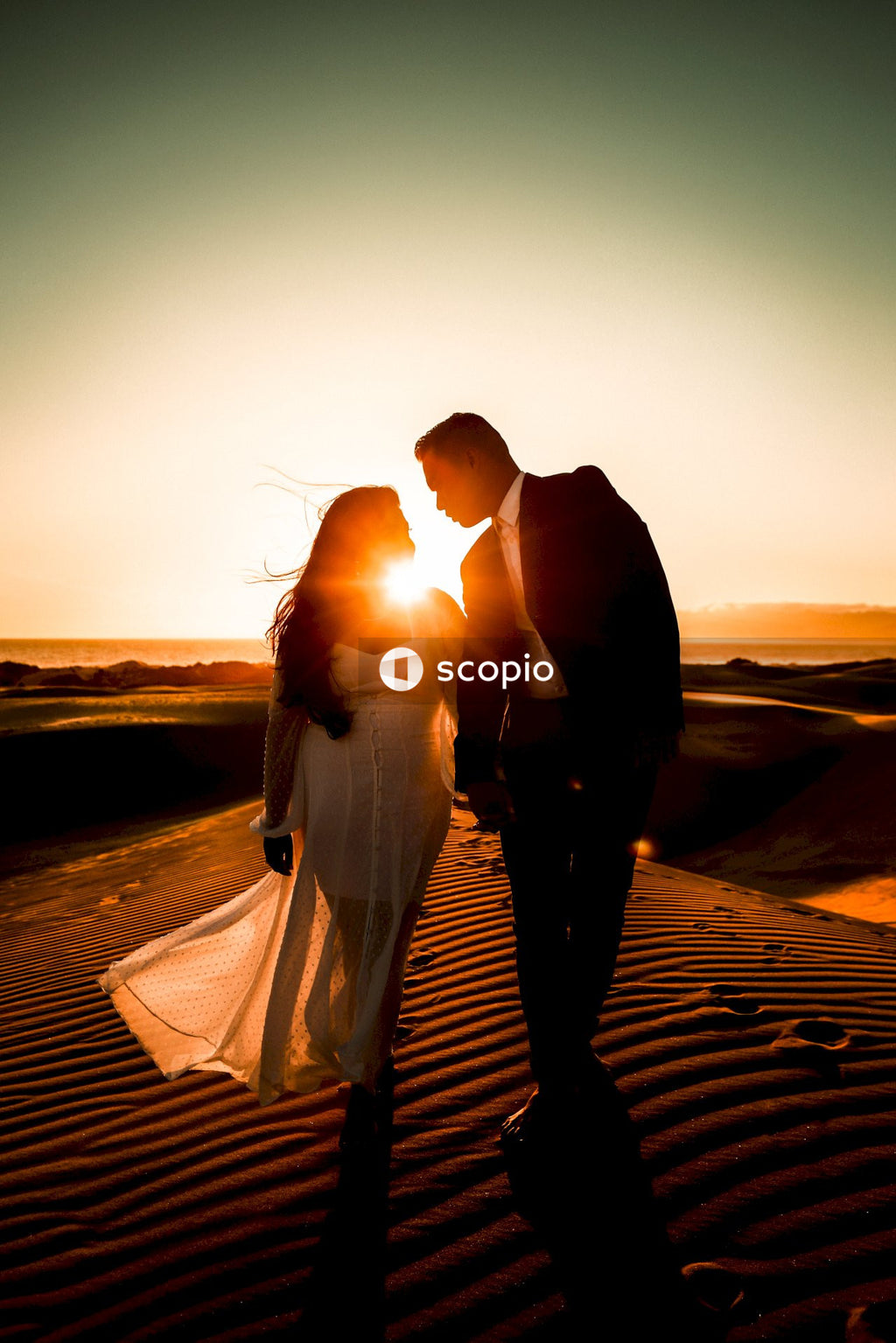 Man and woman kissing on brown sand during sunset