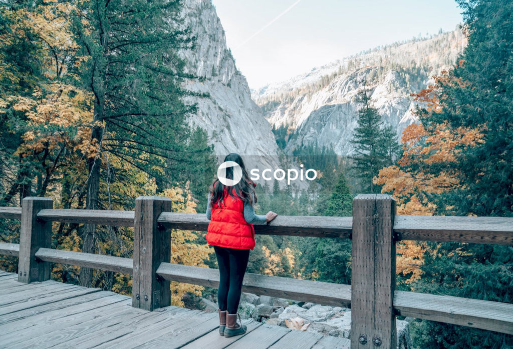 Woman in red long sleeve shirt and black pants standing on brown wooden bridge