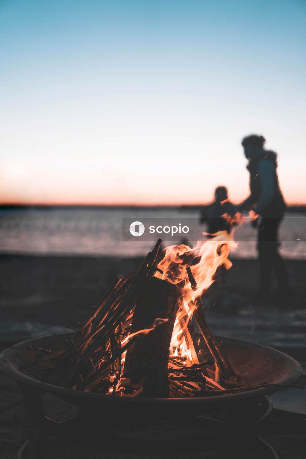 Man and woman standing near bonfire during sunset