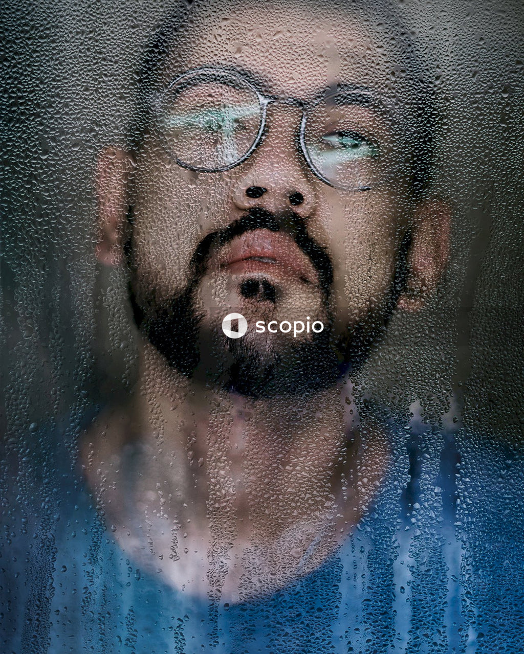 Reflection of man wearing blue top and eyeglasses in wet mirror
