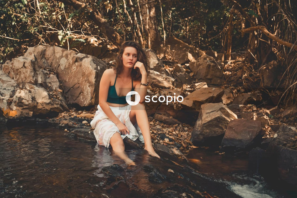 Woman in blue tank top and white shorts sitting on rock in river