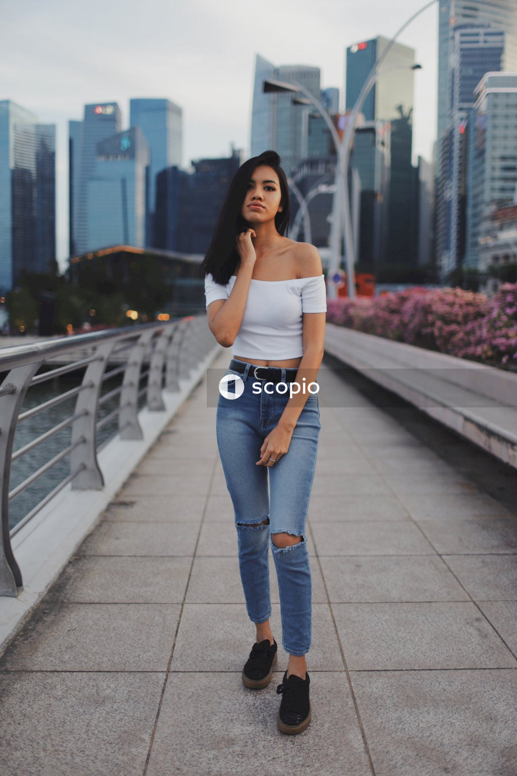 Woman in light tank top and blue denim jeans standing on gray concrete bridge