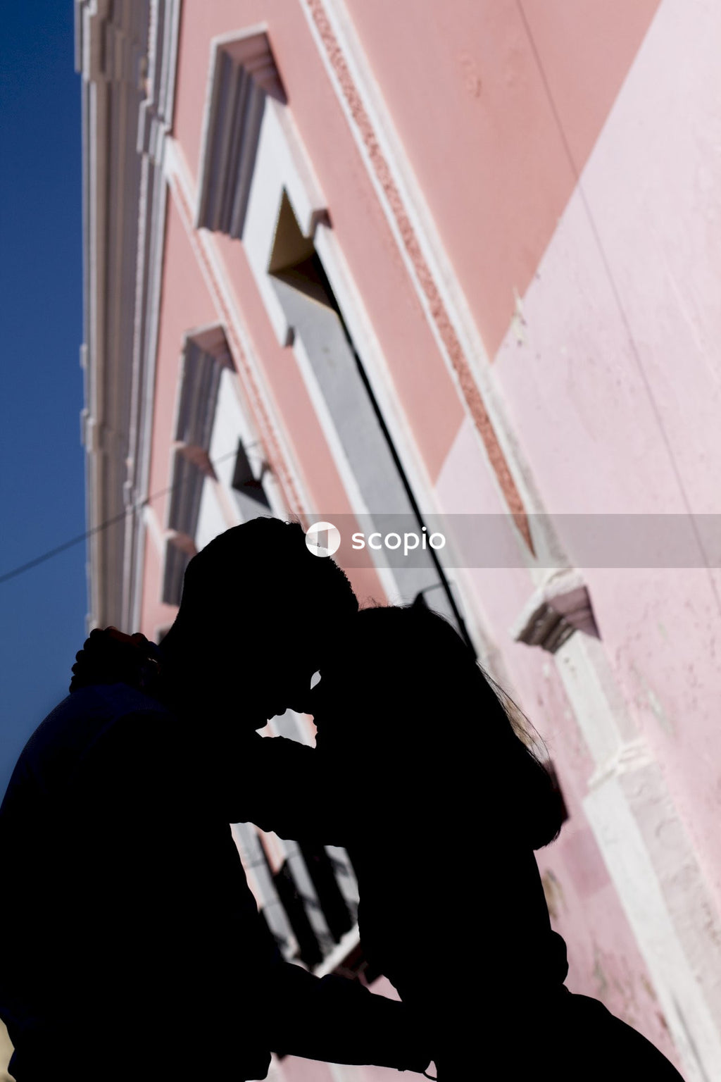 Silhouette of couple kissing against a pink building outdoor