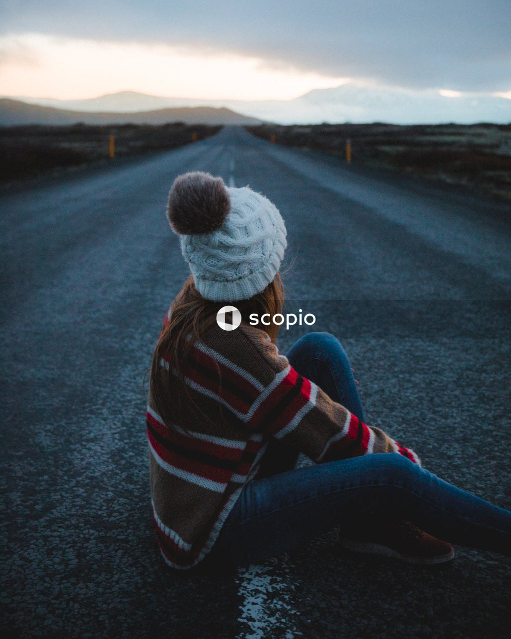 Person in striped hoodie and blue denim jeans sitting in the middle of the road