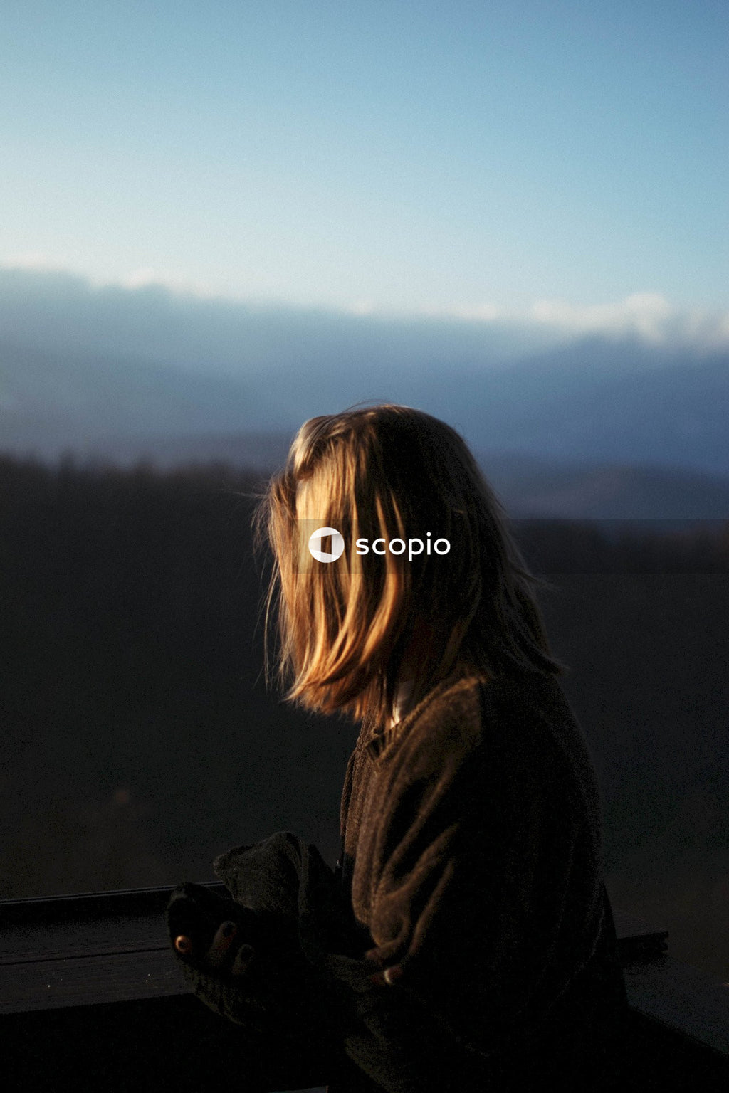 Side view of young blonde woman standing outdoor in wilderness at sunset