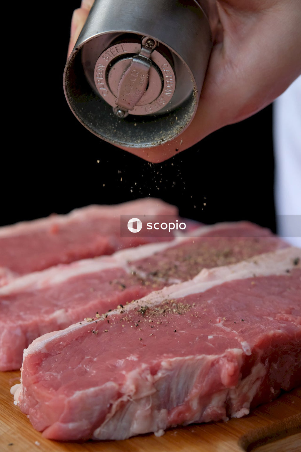 Person grinding pepper over raw meat