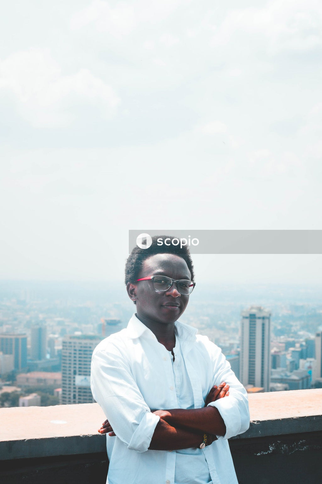 Man standing with arms folded on a balcony overlooking the city