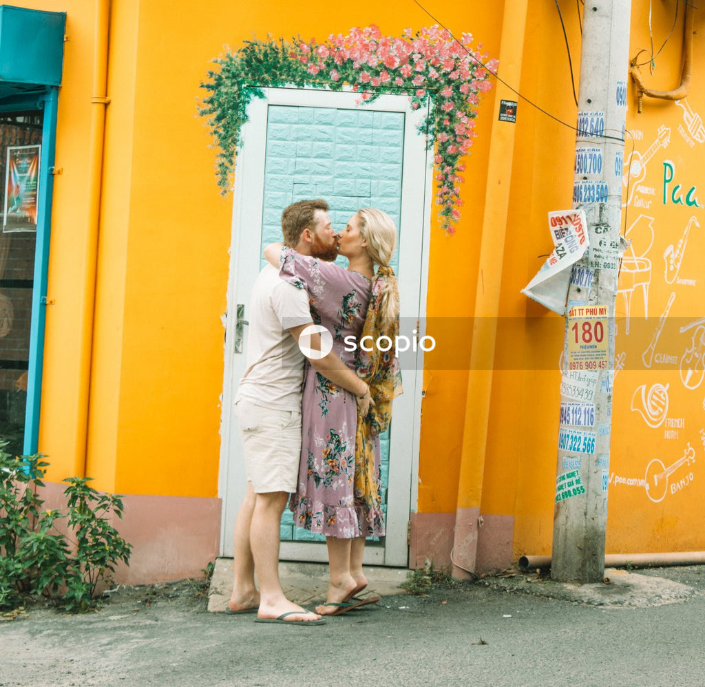 Man and woman kissing beside a yellow wall on street