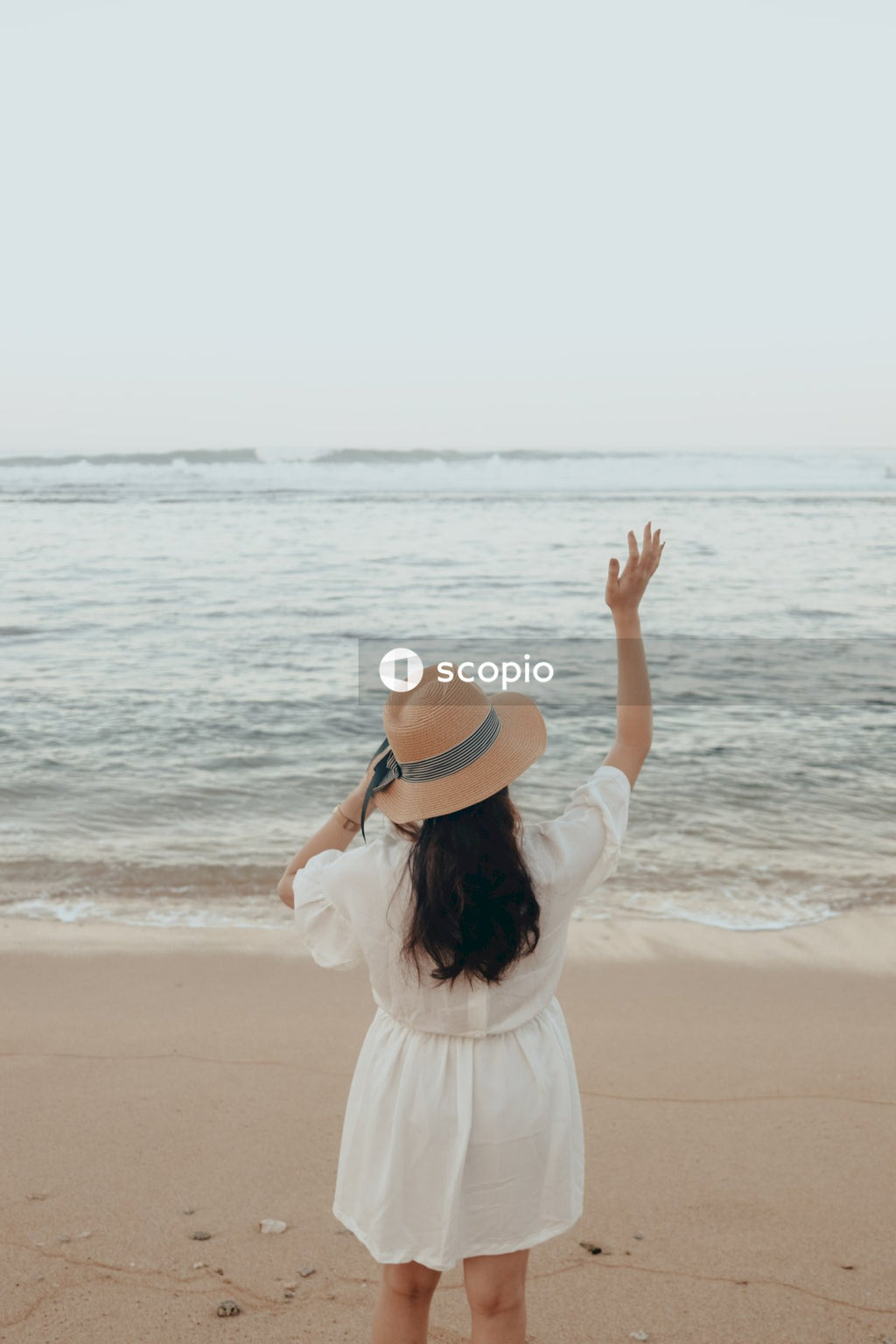 Woman in white dress wearing brown fedora hat standing on beach